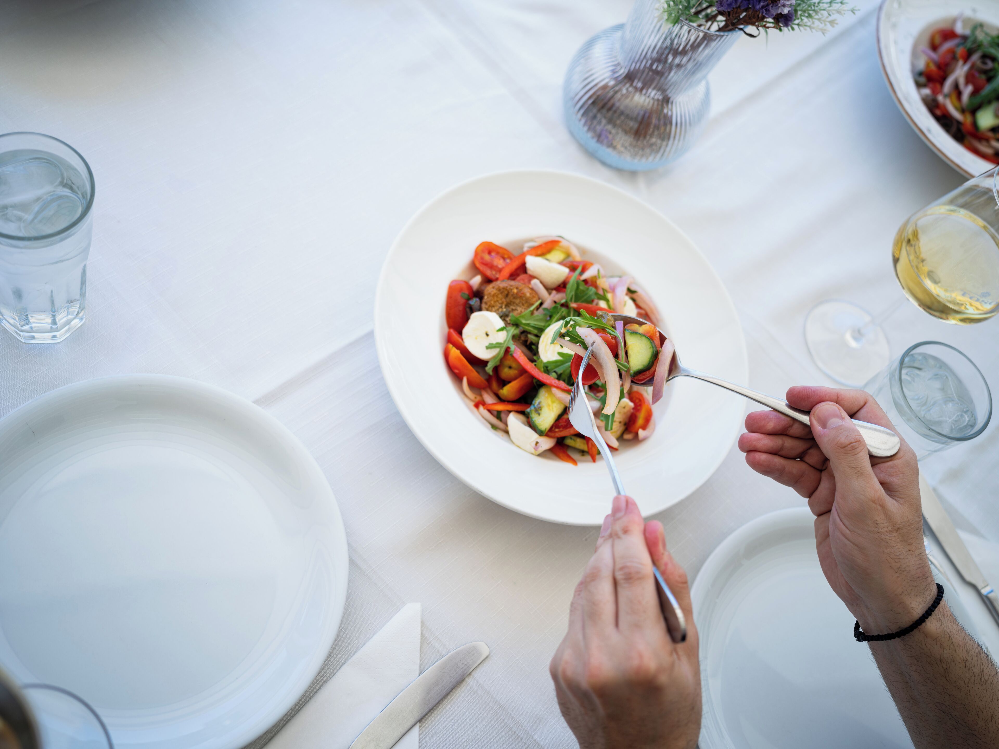 A dining table with a plate of salad, a glass of water, and a wine glass.