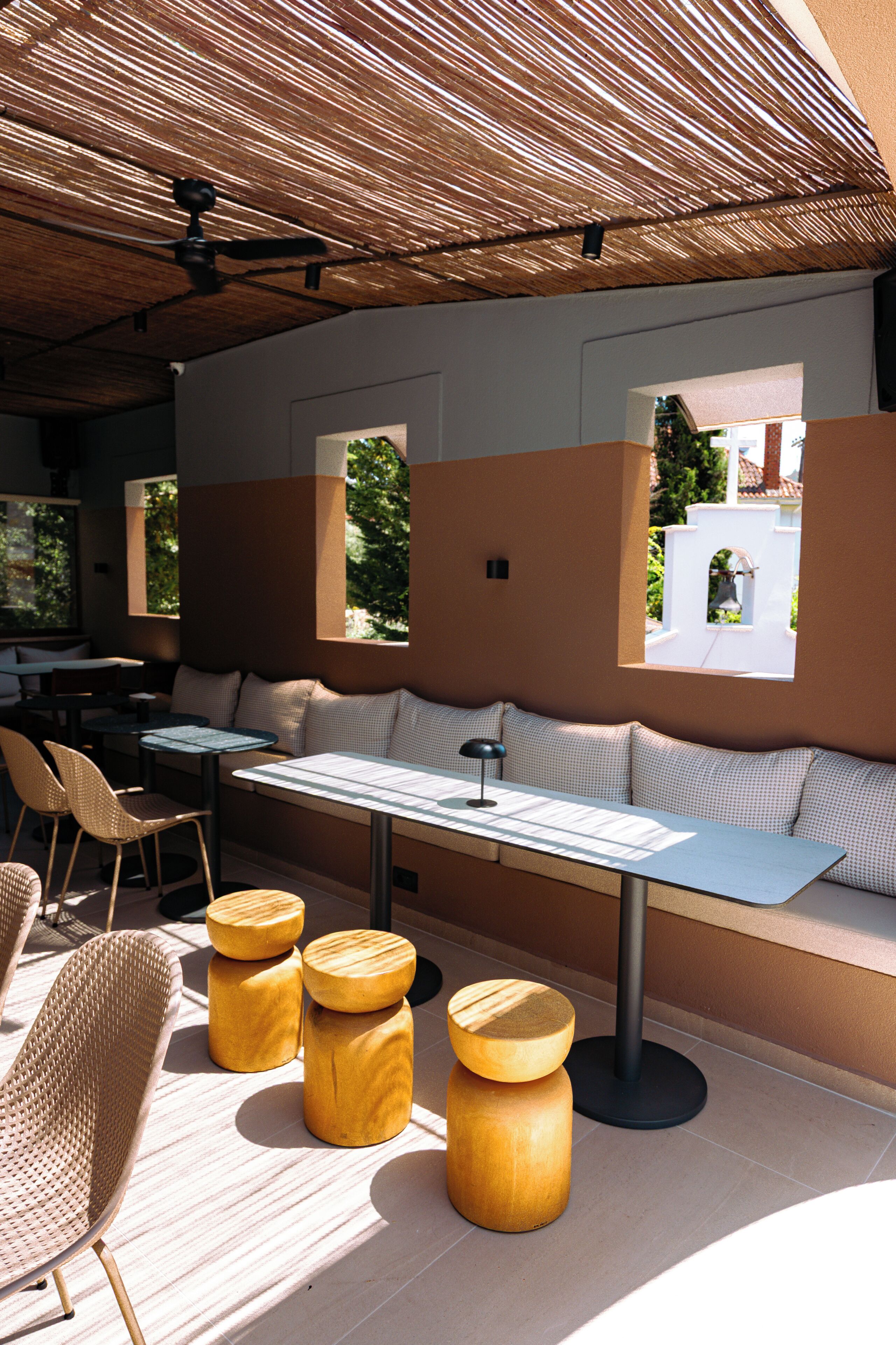A modern outdoor seating area with a thatched roof, cushioned benches, and wooden stools.