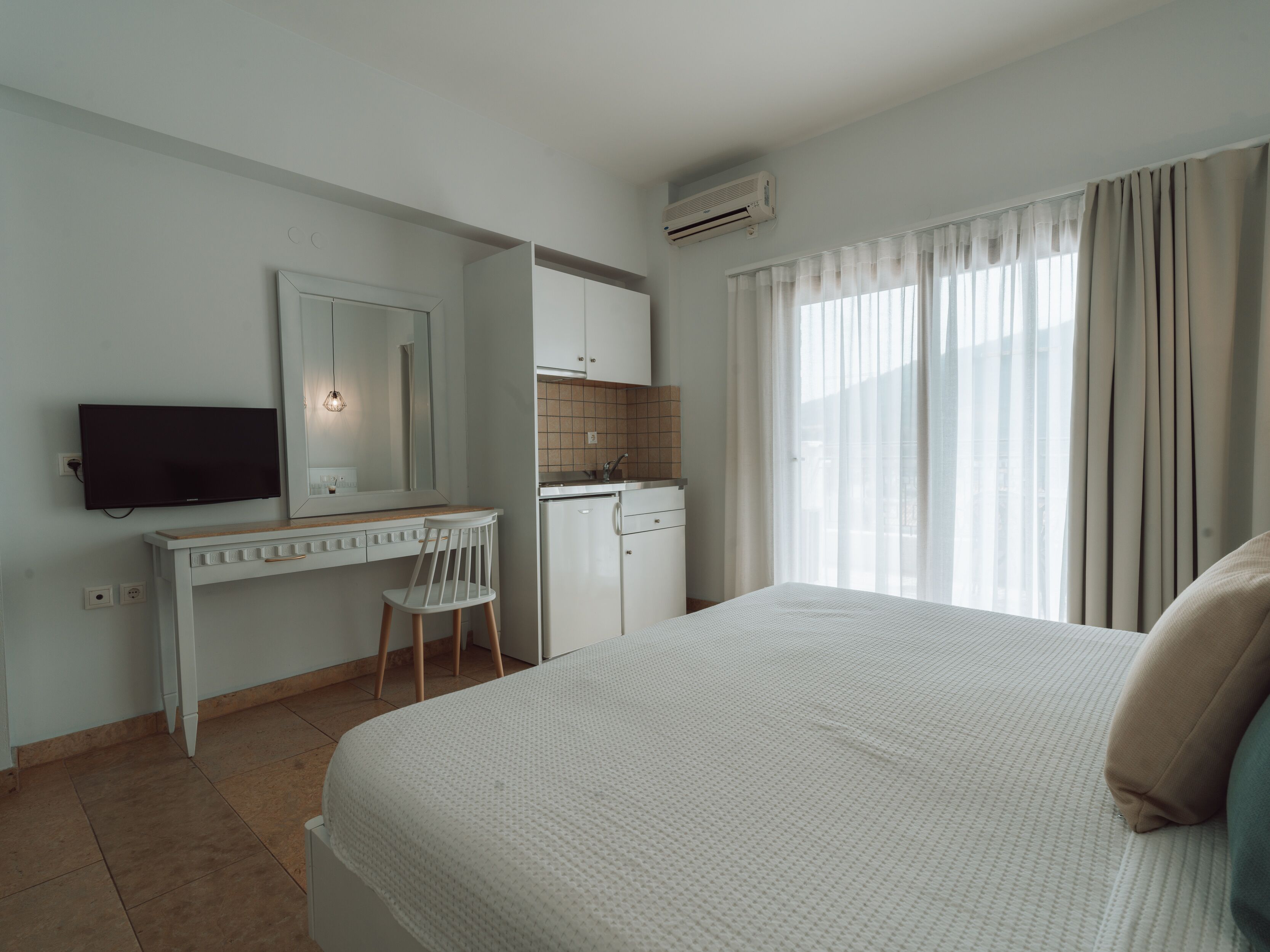 A bedroom with a bed, a desk, a chair, a television, a wardrobe, and a window with curtains.