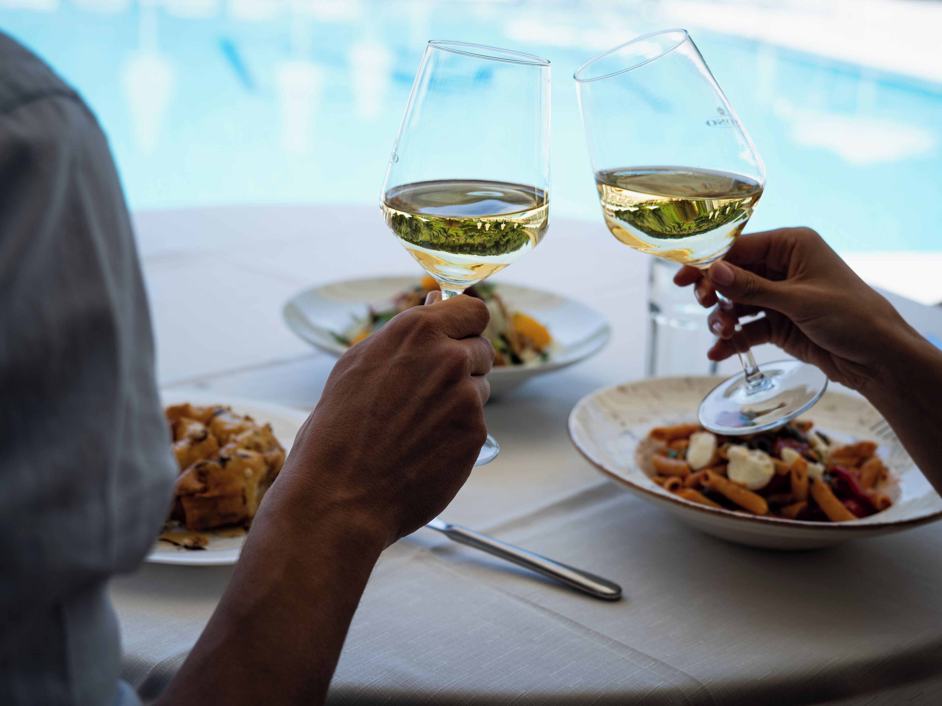 Two people toasting with wine glasses at a table with plates of food.