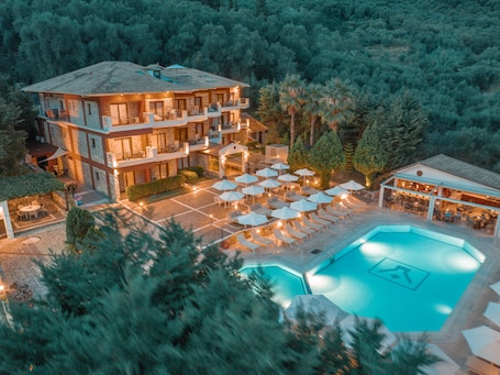 A multi-story hotel with a swimming pool, outdoor seating, and a forested backdrop.