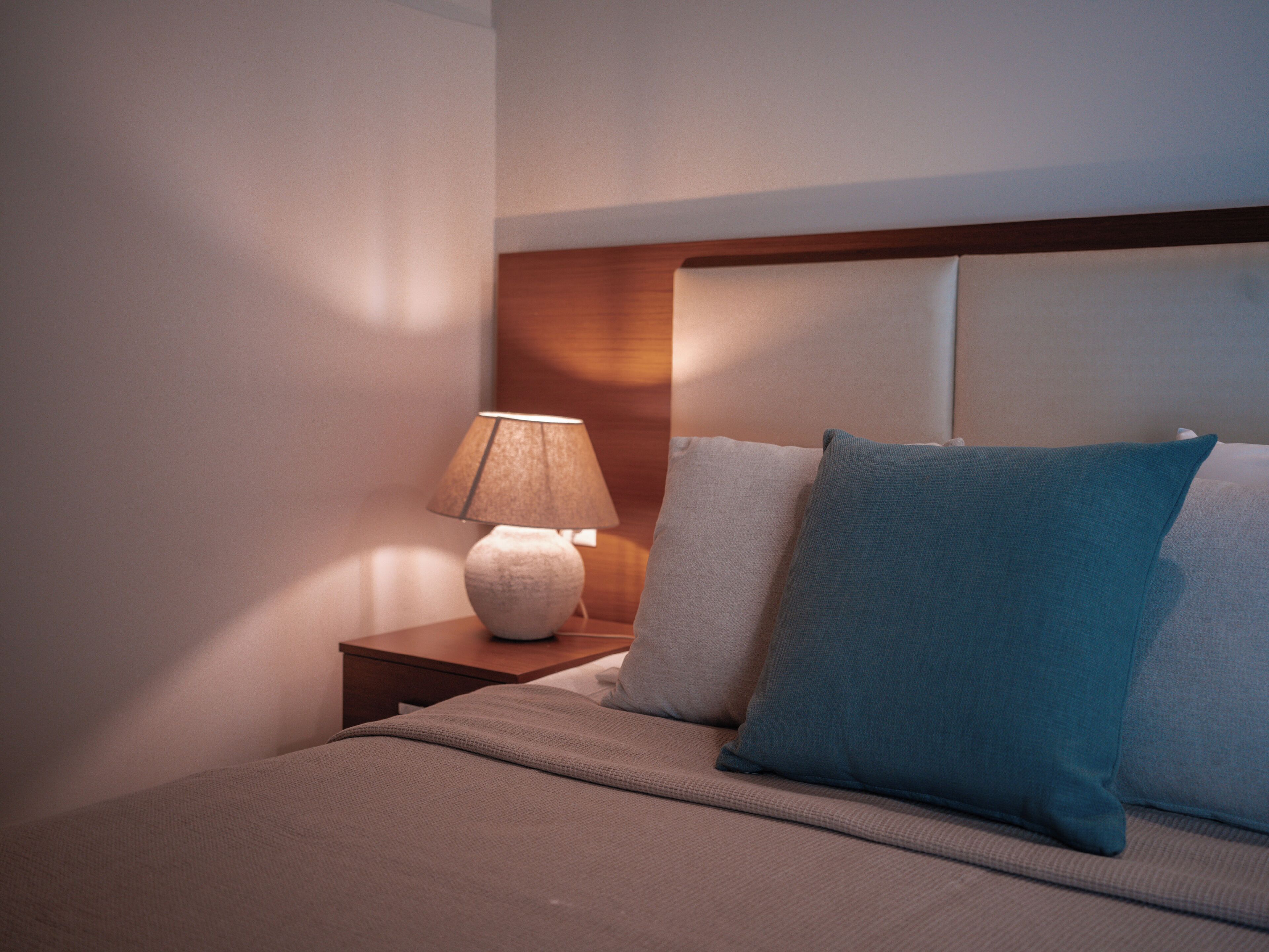 A neatly made bed with a headboard, a bedside lamp, and two pillows.