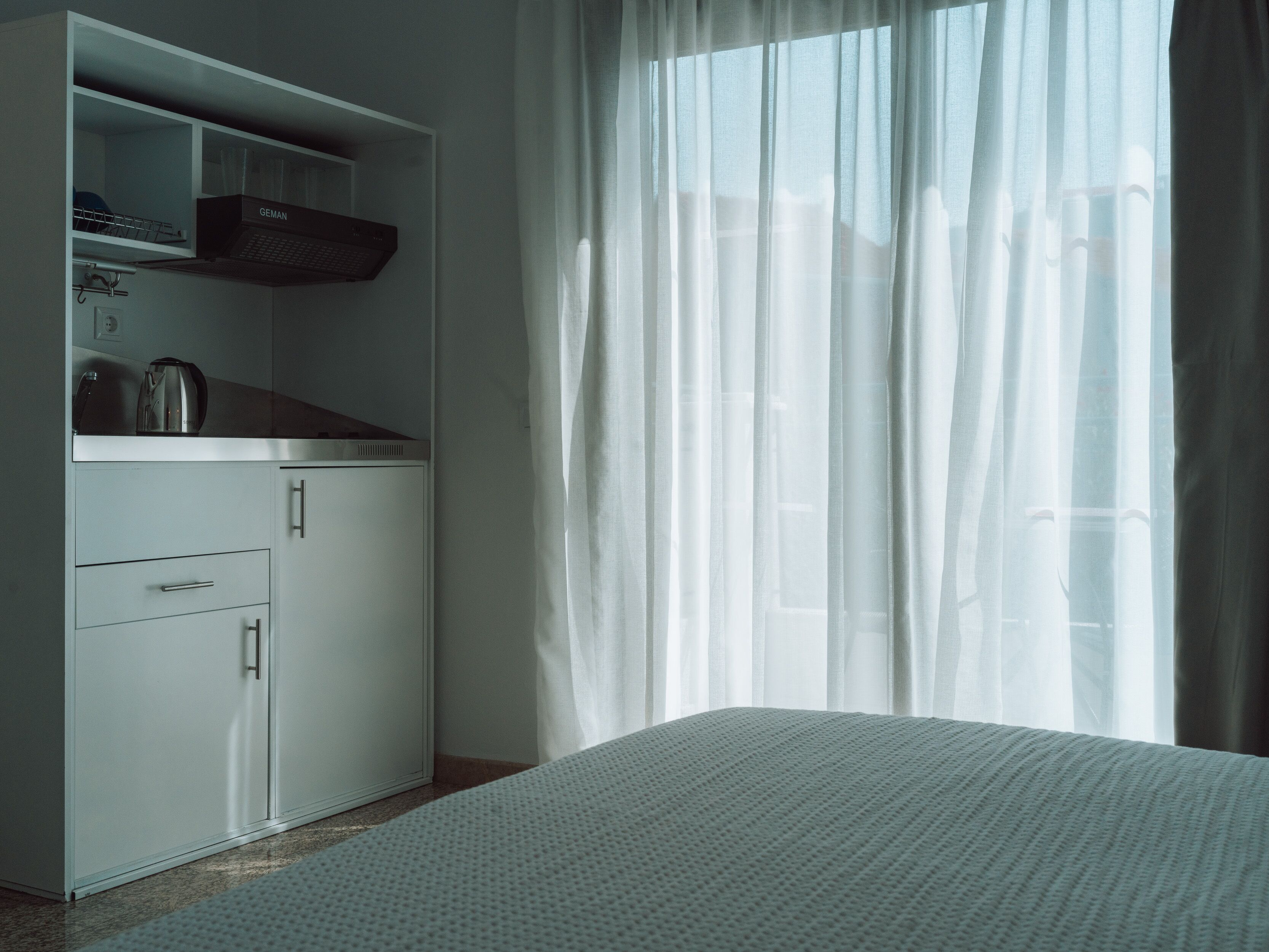 A bedroom with a bed, a wardrobe, and a window with sheer curtains.