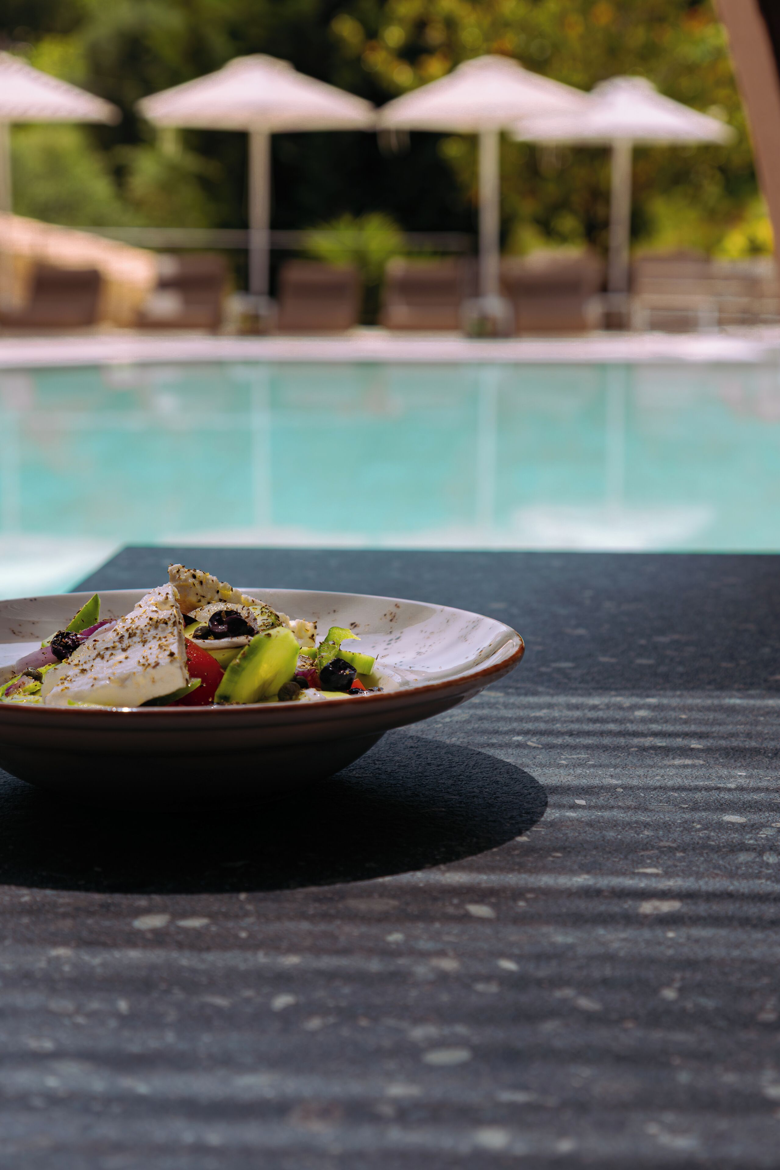 Un plato de comida sobre una mesa cerca de una piscina con sombrillas al fondo.