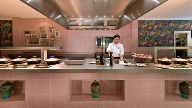 A modern kitchen with pink tiles, stainless steel appliances, and decorative vases.