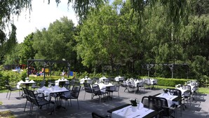 An outdoor dining area with tables and chairs arranged in rows, surrounded by lush greenery and trees. - Van der Valk Hotel Nazareth - Gent (Nazareth)