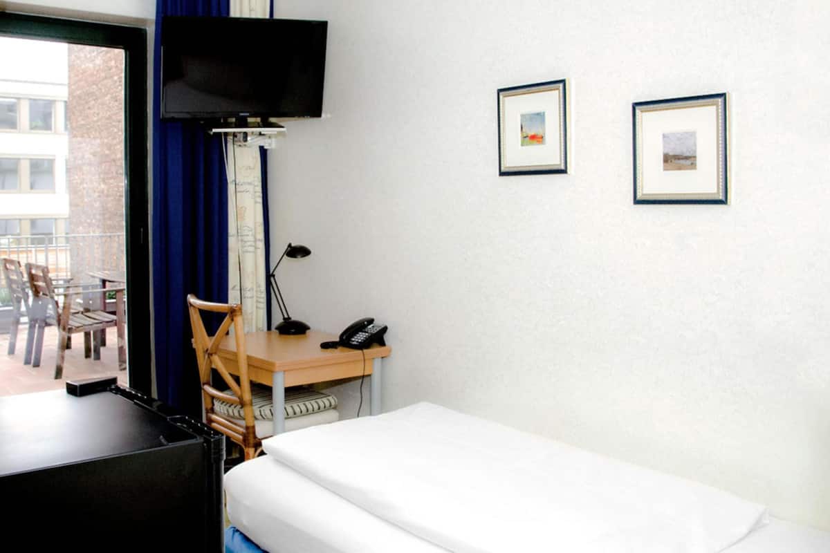 Habitación de hotel con cama, escritorio, silla y televisión montada en la pared.