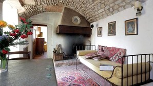 Un salon chaleureux avec un plafond en pierre, une cheminée, un canapé agrémenté de coussins et une table à manger ornée d’un vase de fleurs.