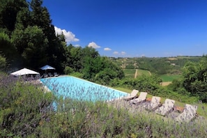 A pool with lounge chairs and a tent, surrounded by greenery and hills. - Il Castello di Bibbione (San Casciano in Val di Pesa)