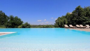 Une piscine d’un bleu éclatant, avec des chaises longues sur le côté droit et des arbres en arrière-plan.