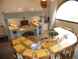 Een eethoek met een open haard, een ronde tafel gedekt voor een maaltijd, en een raam dat natuurlijk licht biedt.