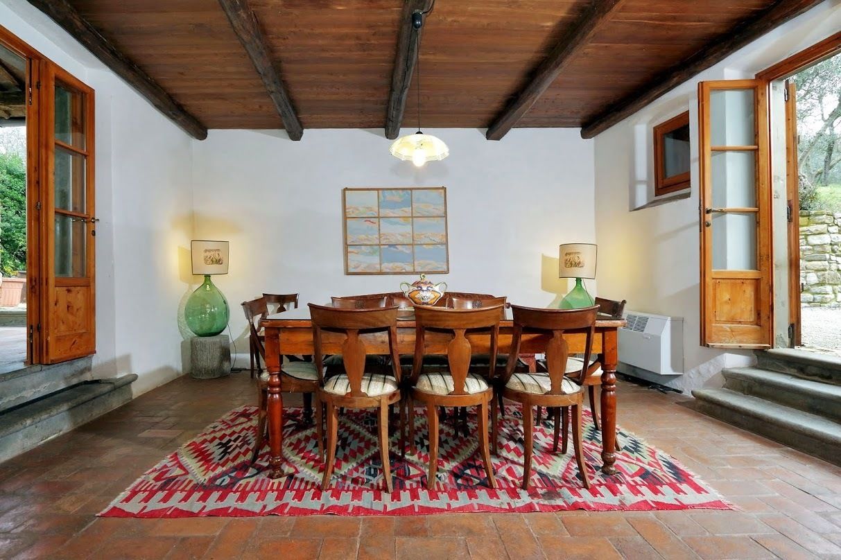 A dining area with a wooden table and chairs, a patterned rug, and a ceiling with exposed beams.