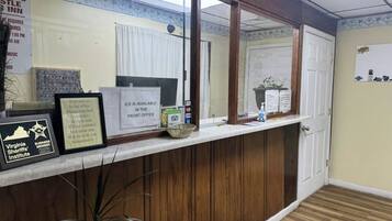 A reception area with a wooden counter, framed certificates, a sign indicating ice availability, and a door in the background.