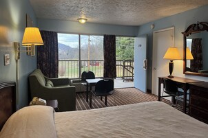 Quarto de hotel com cama, escrivaninha, cadeira, abajur e vista para o exterior.