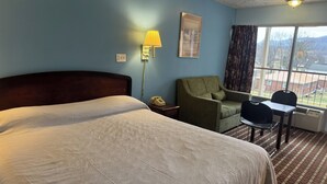 Ett hotellrum med en stor säng, ett skrivbord, en stol, en lampa och ett fönster med utsikt.