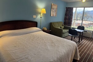 Quarto de hotel com uma cama grande, uma escrivaninha, uma cadeira, um abajur e uma janela com vista.