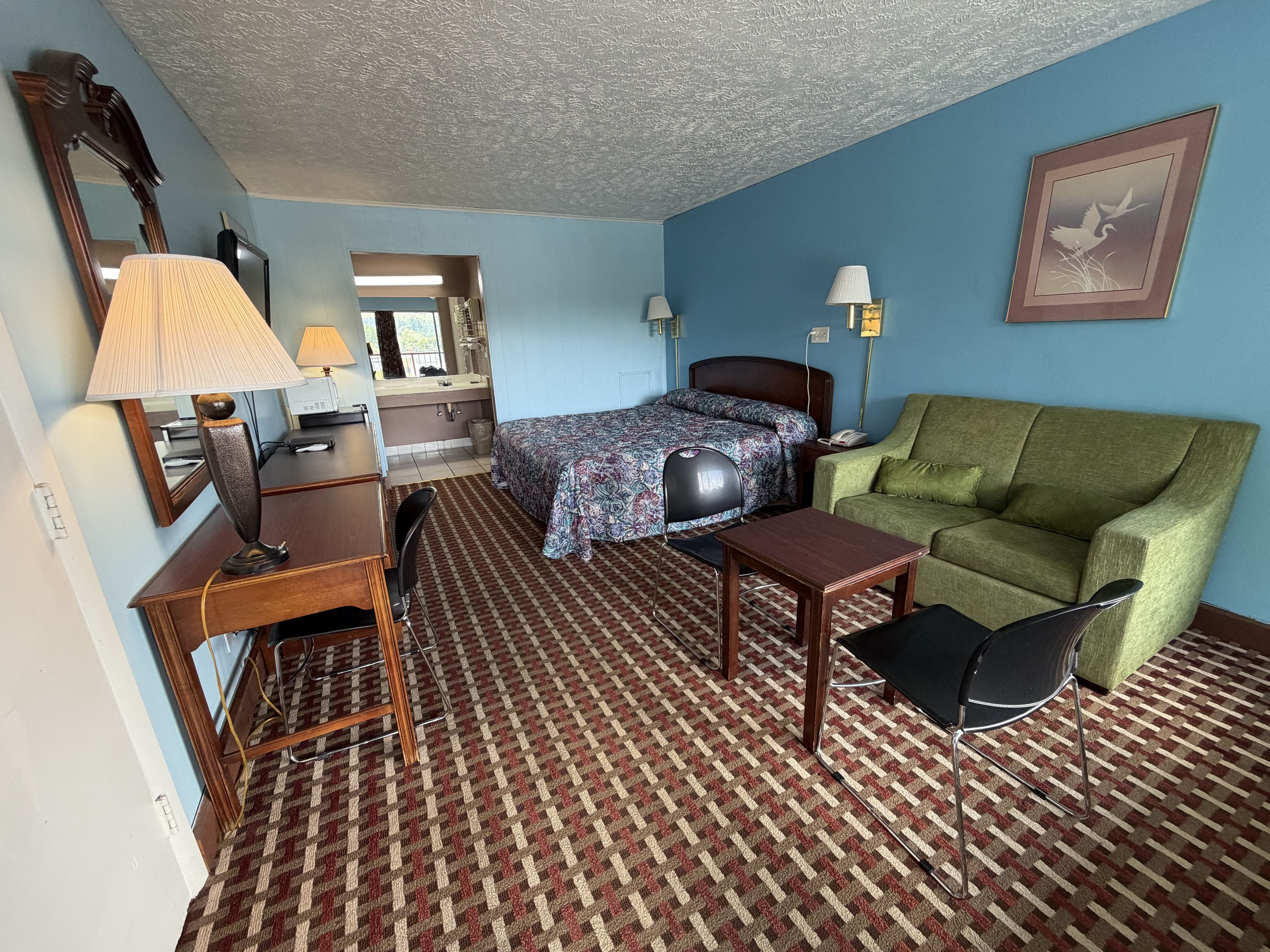 A hotel room with a bed, a desk, a chair, a green sofa, and a patterned carpet.