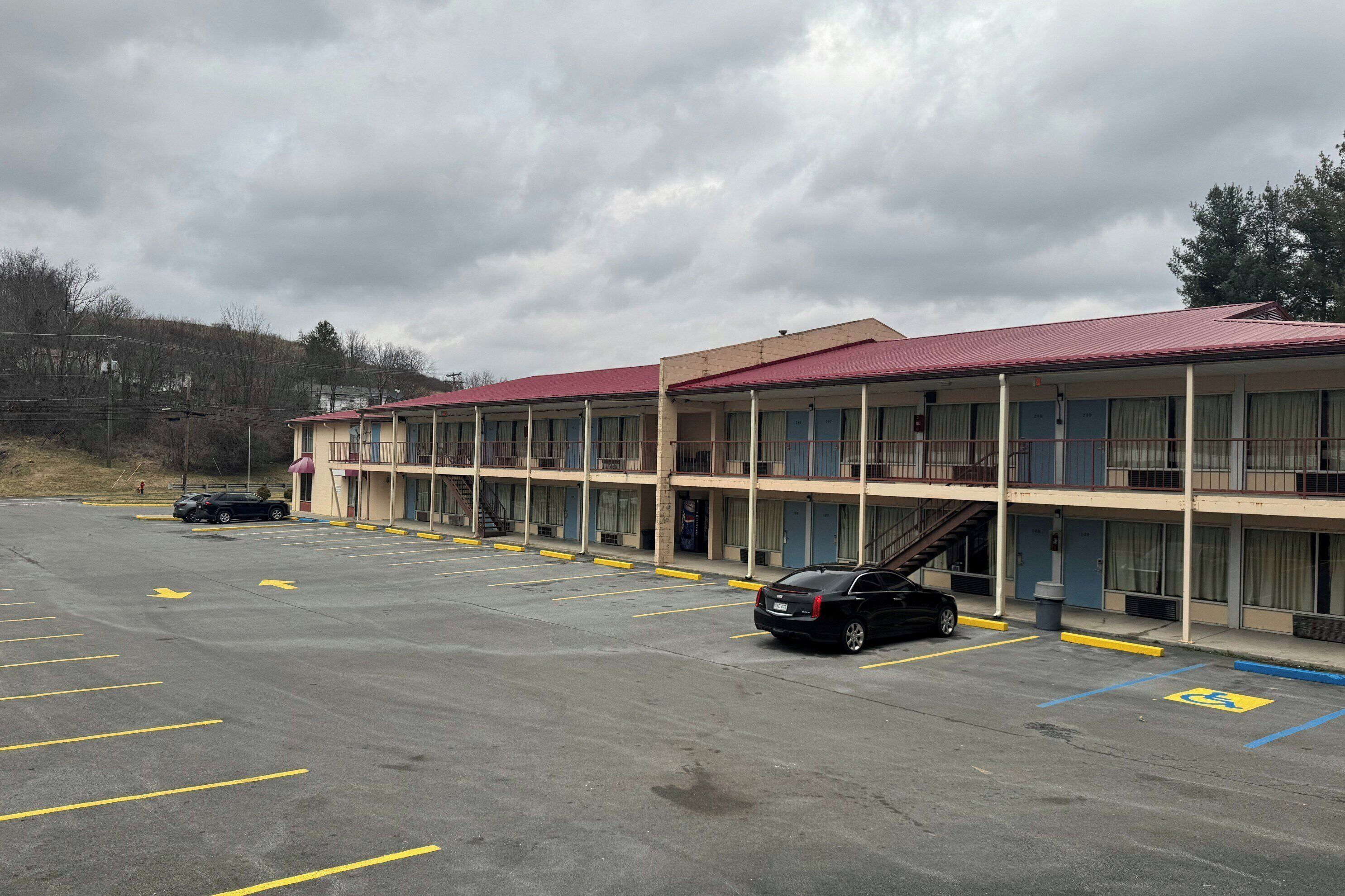 Et motel med rødt tag, flere etager og en parkeringsplads med afmærkede parkeringsfelter.