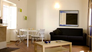 Ein Wohnzimmer mit Holzboden, weißen Wänden, einem schwarzen Sofa, einem weißen Tisch und einem gerahmten Bild.