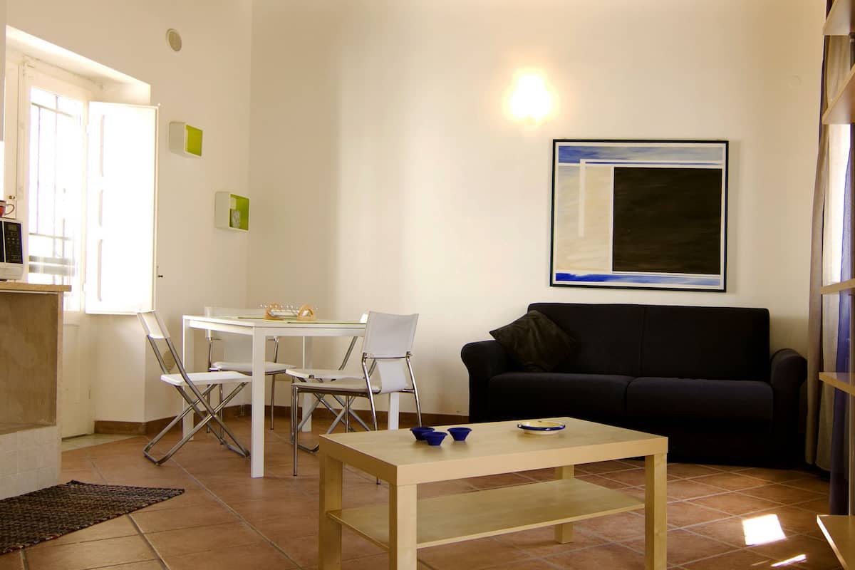 A living room with a wooden ceiling, white walls, a black sofa, a white table, and a framed picture.