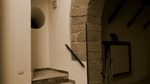 Eine Steintreppe führt zu einer oberen Ebene, mit einem Blumentopf auf der Zwischenebene und einem kleinen, runden Fenster links.