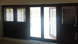 Ein Zimmer mit einem großen Fenster, das mit Holzklappläden und einem Ventilator auf der rechten Seite versehen ist.