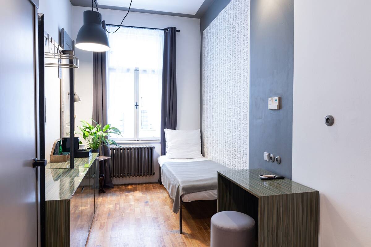 Een moderne slaapkamer met een bed, nachtkastje, lamp en een raam met gordijnen.
