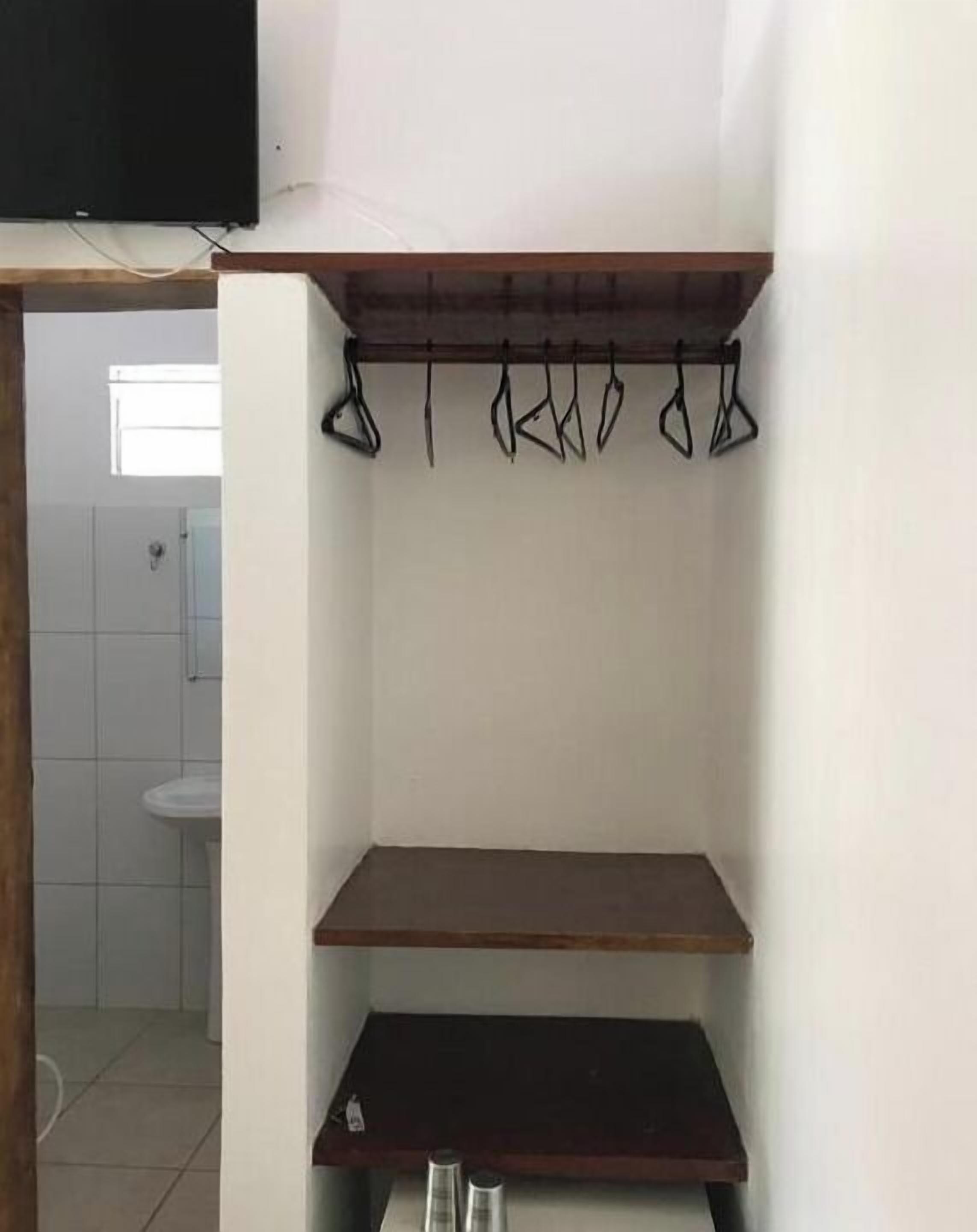 A room with a wooden shelf, a hanging rack, and a sink in the background.