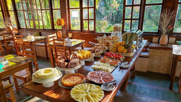 A buffet table with various food items and a view of a lush garden through large windows. - Pousada Tropical Arraial (Porto Seguro)