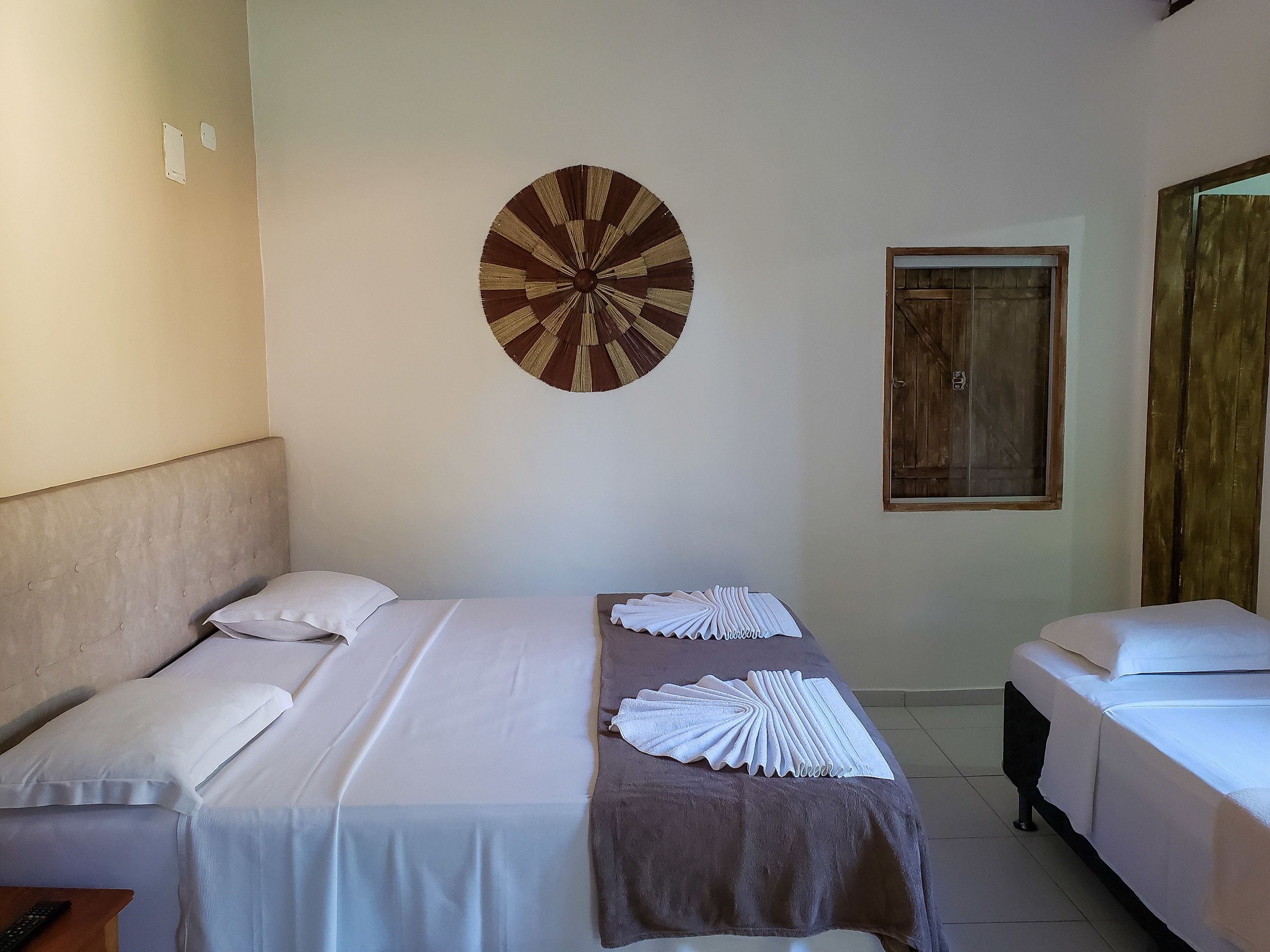 A hotel room with two beds, a round wall decoration, a wooden door, and a window.