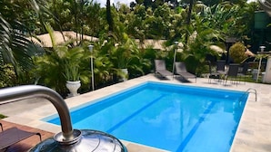 A swimming pool with a metal grill, surrounded by wooden decking and lounge chairs, with lush greenery in the background. - Pousada Tropical Arraial (Porto Seguro)