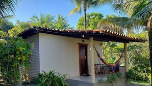 A small, single-story building with a tiled roof, a wooden door, and a porch with a hammock. - Pousada Tropical Arraial (Porto Seguro)