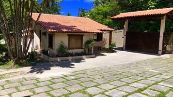 Una propiedad residencial con camino de entrada pavimentado, un pequeño jardín con palmeras y una casa con techo de tejas rojas.