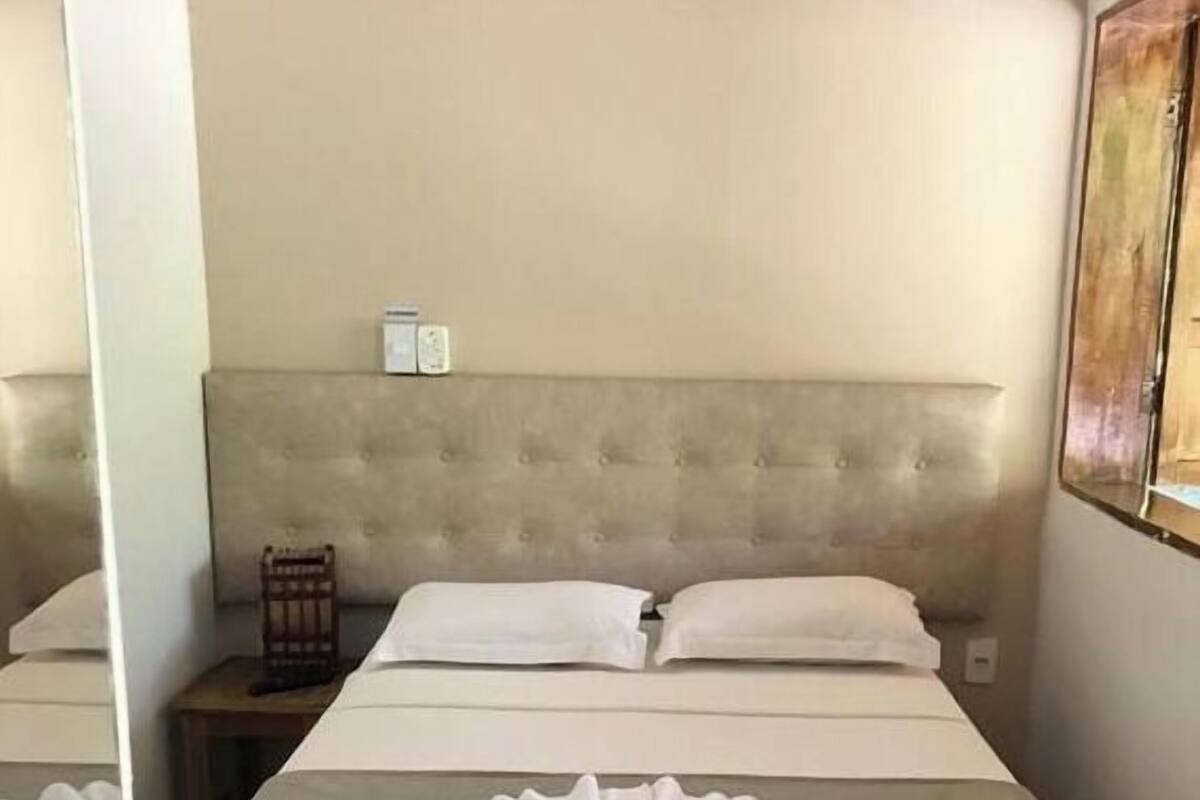 A hotel room with a large bed, a headboard, a nightstand, and a wall-mounted light.