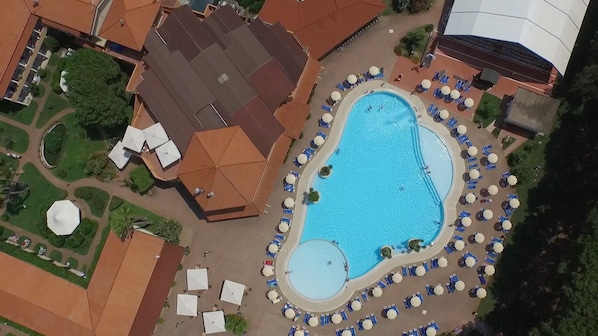An aerial view of a resort with a large swimming pool surrounded by lounge chairs and umbrellas, a covered area with a roof, and a landscaped garden. - Nicotera Beach Village (Nicotera Marina)