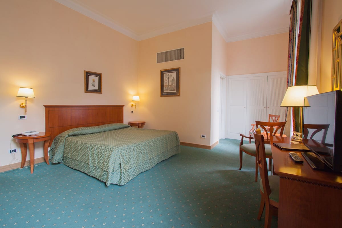 A hotel room with a bed, two bedside tables, a desk with a chair, and a television.