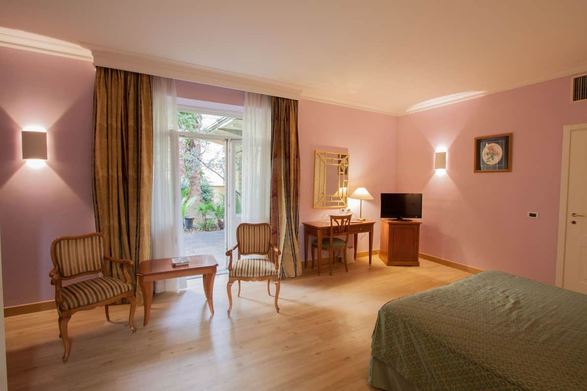 A hotel room with a bed, two chairs, a desk, a television, and a window with curtains.