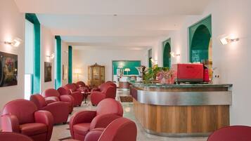 Eine Hotelhalle mit roter Sitzmöbeln, einem Empfangstresen und Türkis-Akzenten an den Wänden.