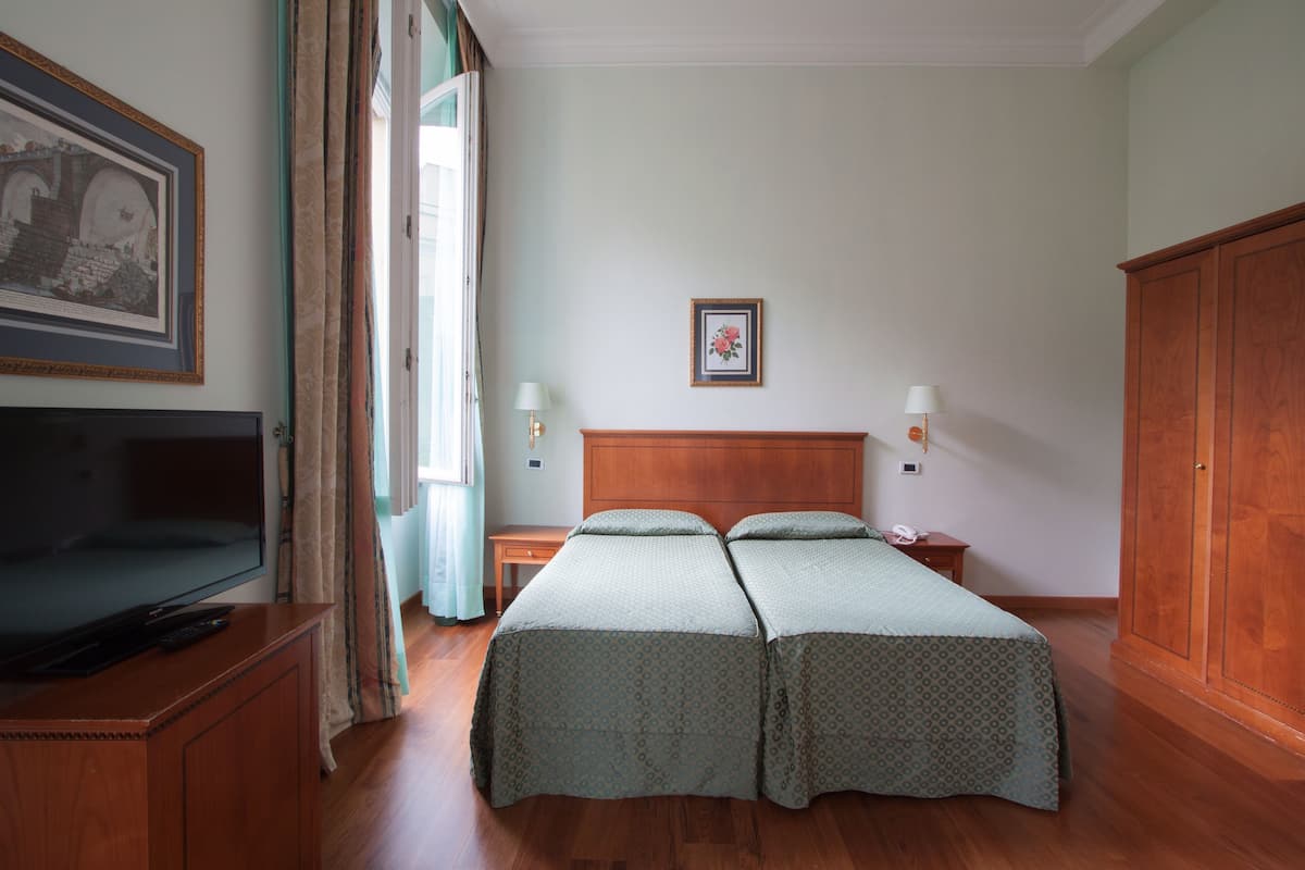 A hotel room with a wooden bed, a television on a wooden cabinet, a bedside table with a lamp, and a wardrobe.
