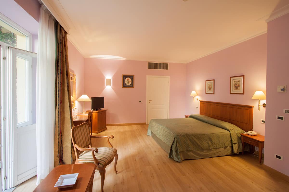 A hotel room with a bed, a desk with a chair, a television, and a window with curtains.