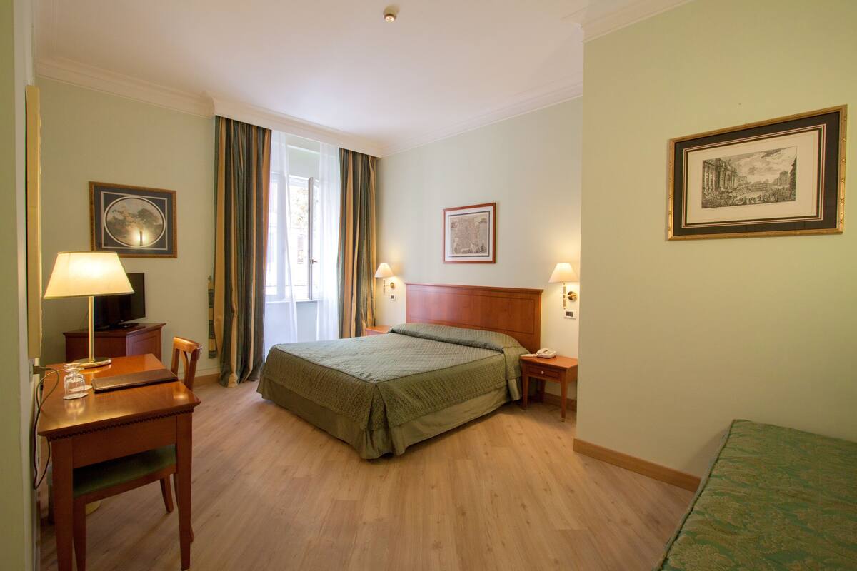 A hotel room with a bed, a desk with a lamp, a chair, and a television.