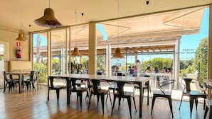 A spacious indoor area with wooden flooring, tables, and chairs arranged for dining. - Camping 3 Estrellas (Gava)