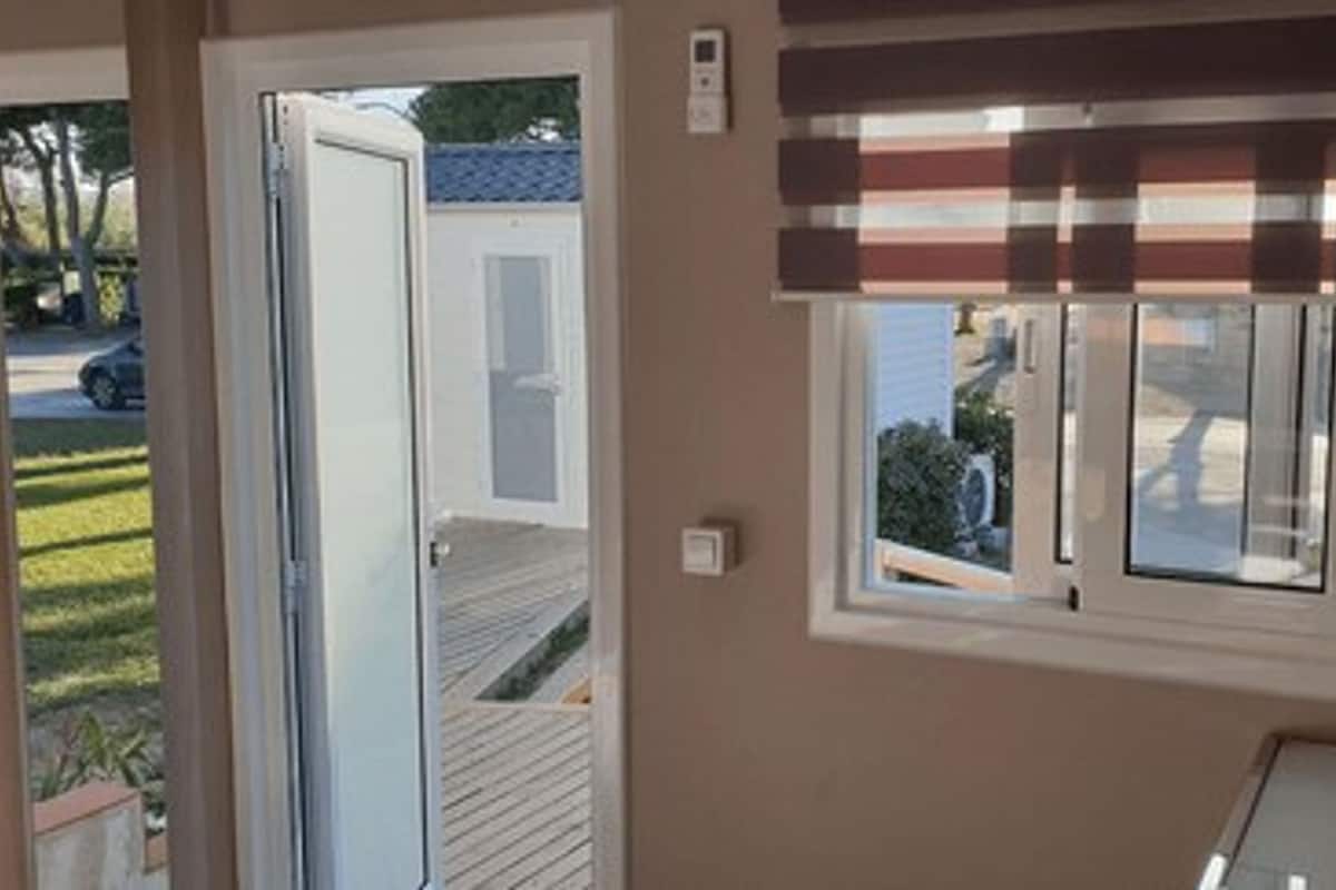 Quarto com porta de vidro deslizante para o exterior, janela com persianas e uma pequena mesa com um livro.