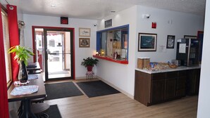 A hotel lobby with a reception desk, a plant, a framed picture, and a refrigerator. - Model Towne Inn (Gwinn)