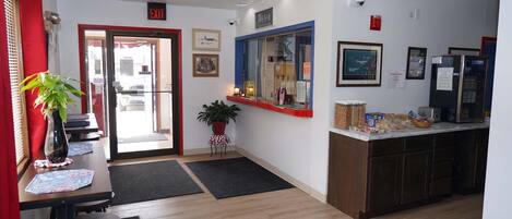 A hotel lobby with a reception desk, a plant, a framed picture, and a refrigerator.