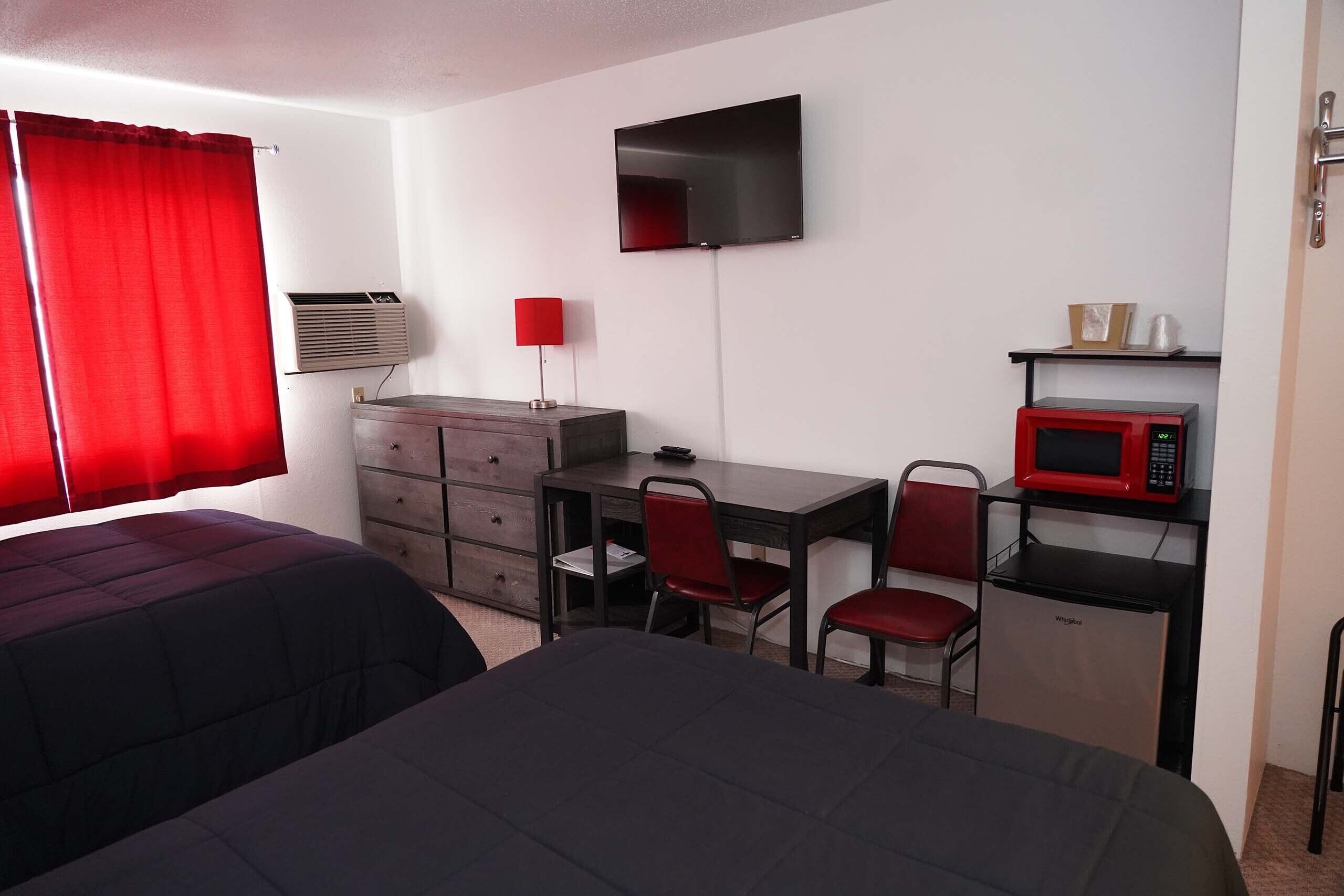 Een hotelkamer met twee bedden, een bureau met een stoel, een televisie, een magnetron en een kleine koelkast.