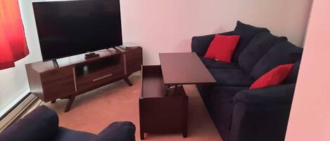 A living room with a dark-colored sofa, a small wooden table, and a TV on a wooden stand.