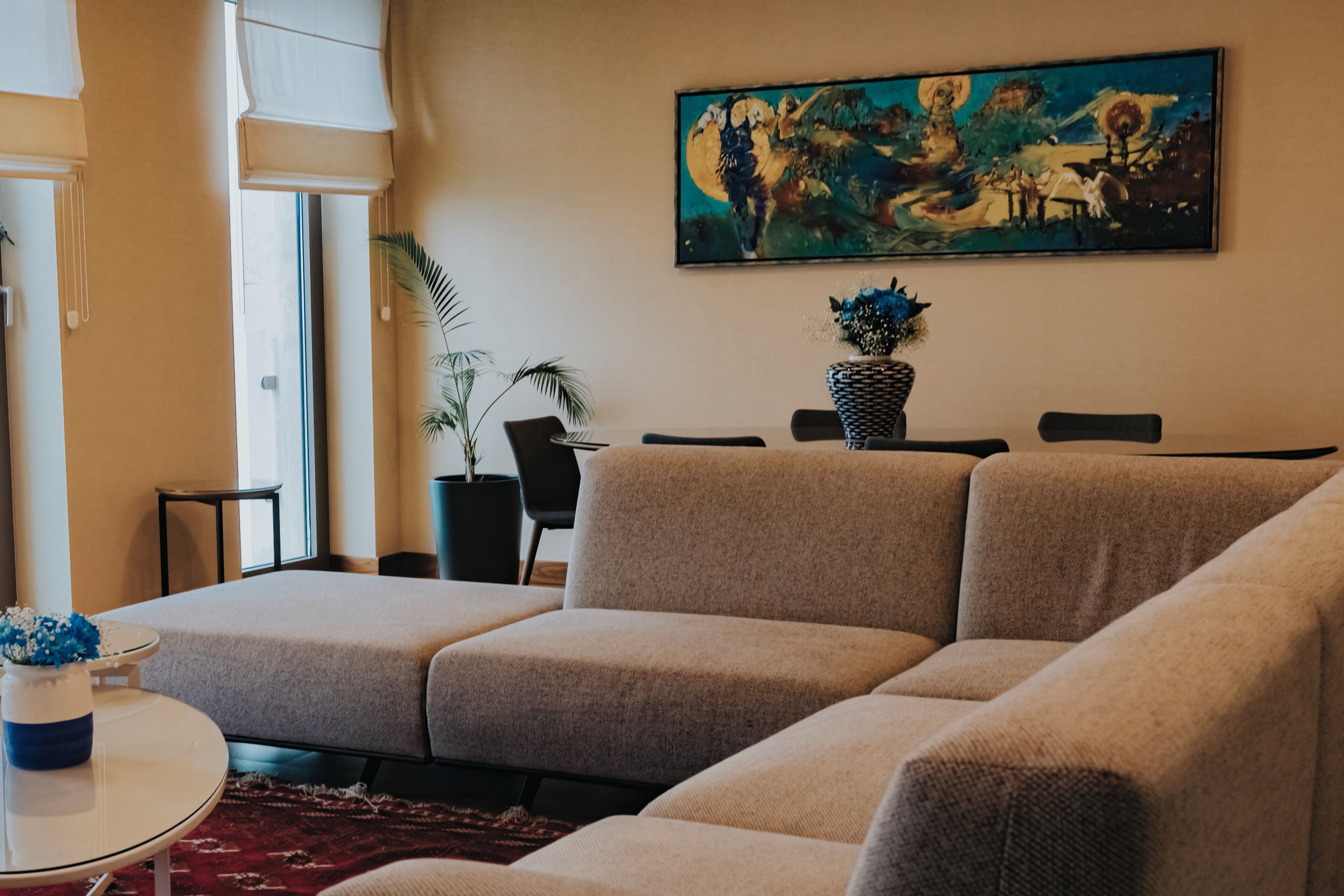Un salon avec un canapé beige, une table à manger avec des chaises, une plante en pot et un tableau accroché au mur.