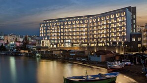 Ein modernes Hotel mit zahlreichen gleichmäßig beleuchteten Fenstern, gelegen an einem ruhigen Ufer mit dort vertäuten Booten.