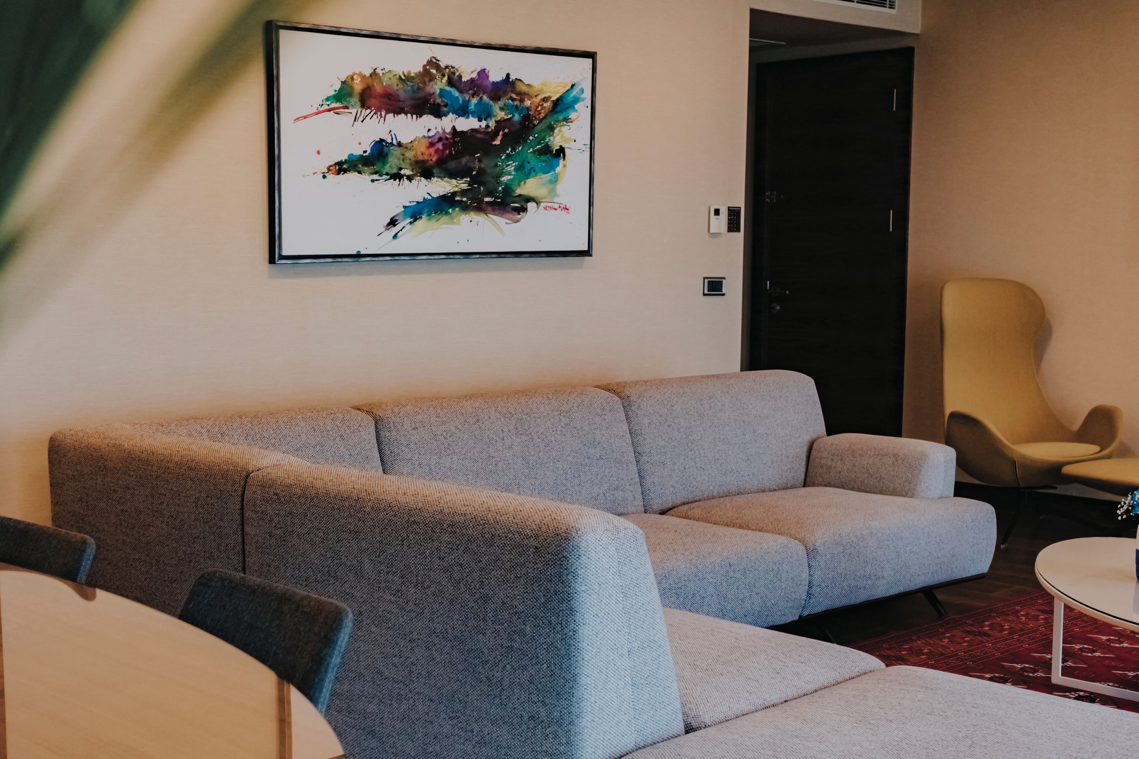 A modern living room with a grey sofa, a round coffee table, and a colorful abstract painting on the wall.